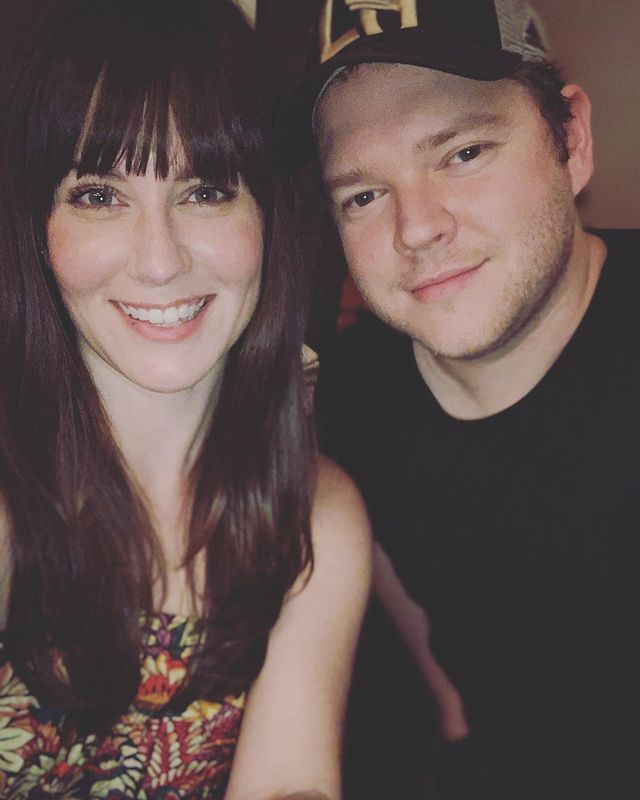 Katie Featherston in a floral print top smiling with Harry Ford in a black t-shirt.